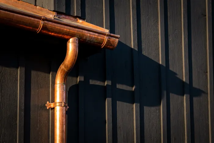 Copper half-round gutter and downspout against dark siding
